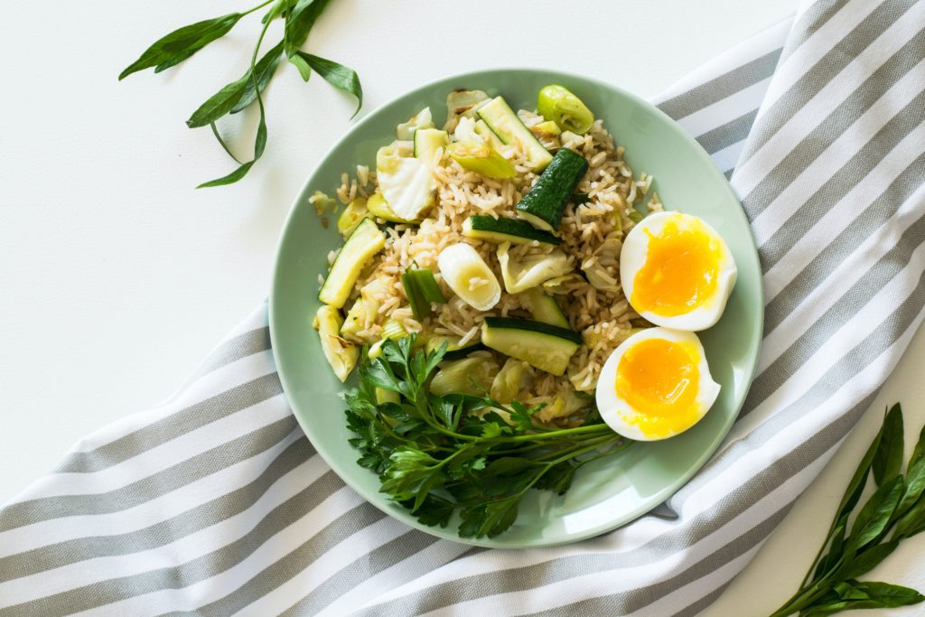 Rice With Poached Egg, Zucchini, And Celery on Round Green Ceramic Plate