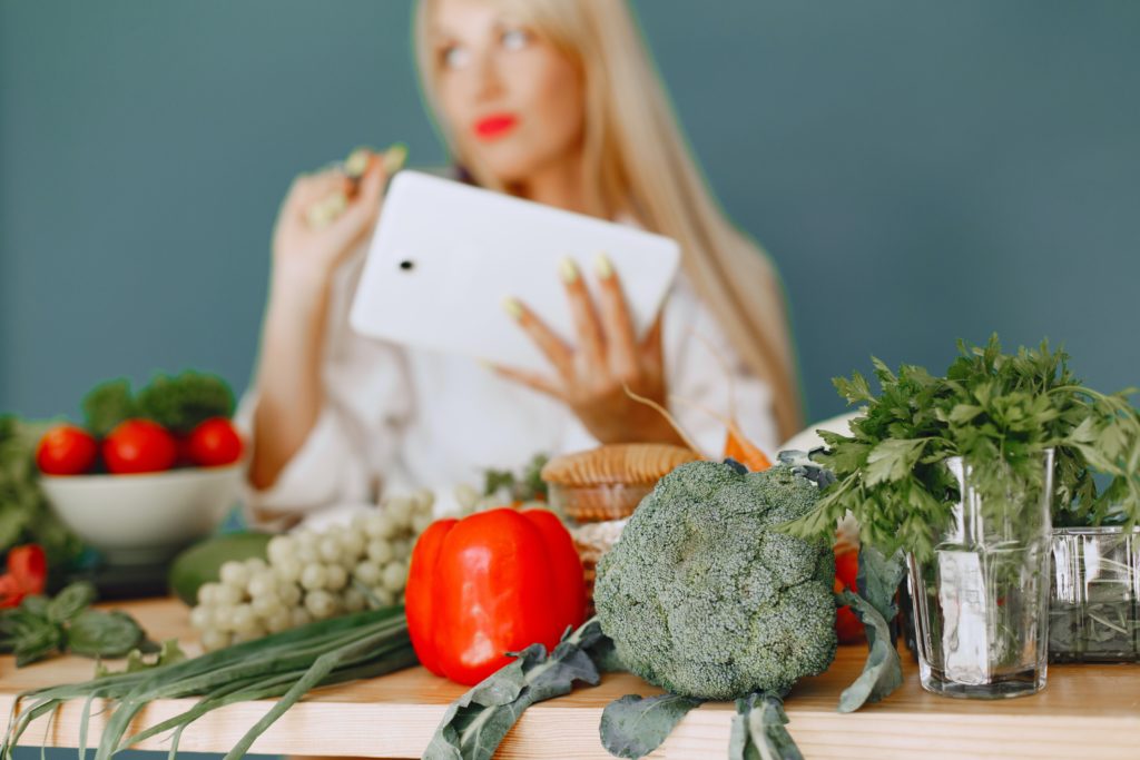 Studio Shot of Vegetables on Table and Woman with Tablet in Background