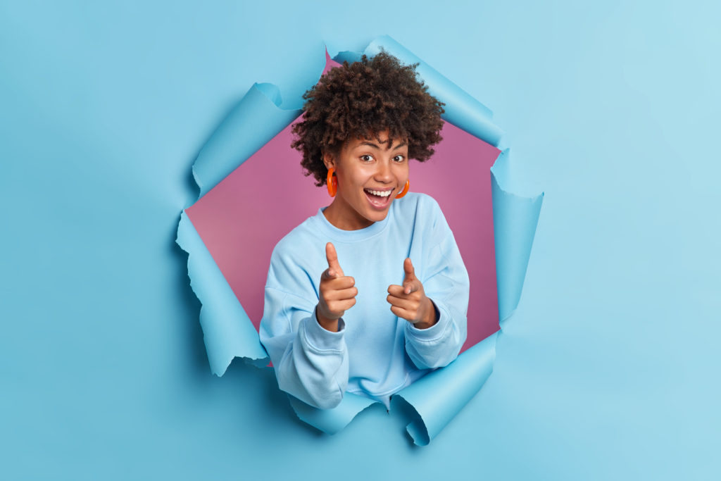 Joyful smiling dark skinned afro American woman points index fingers