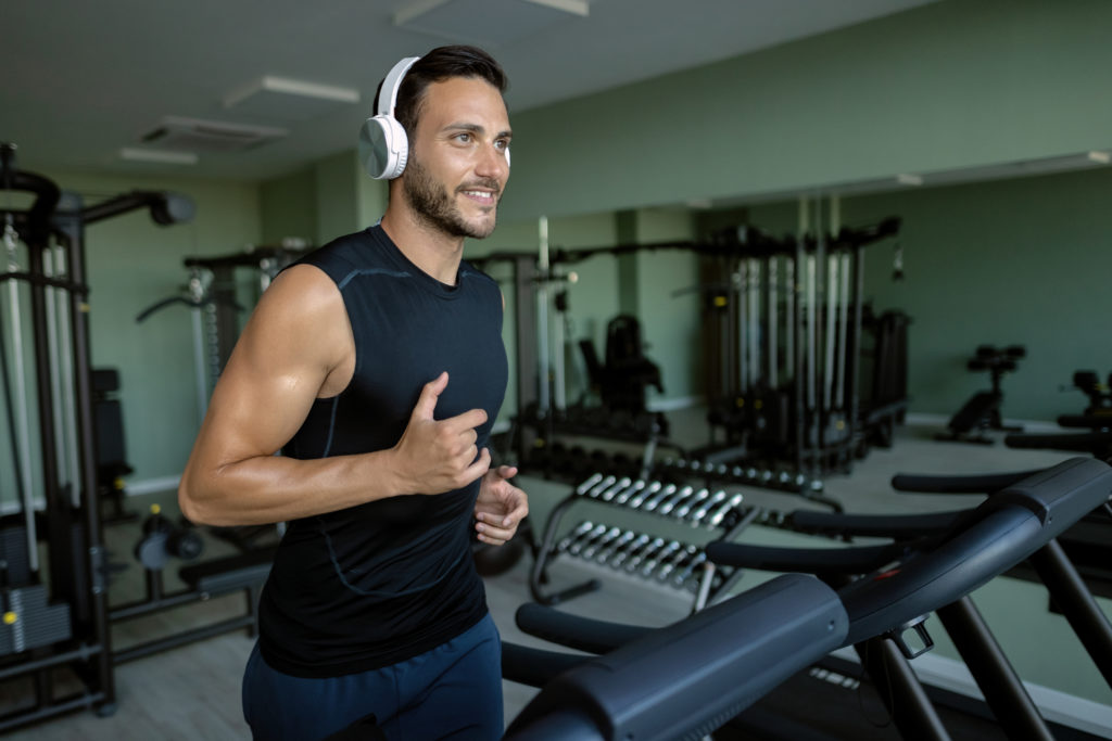 Smiling athletic man running on treadmill while exercising in a gym