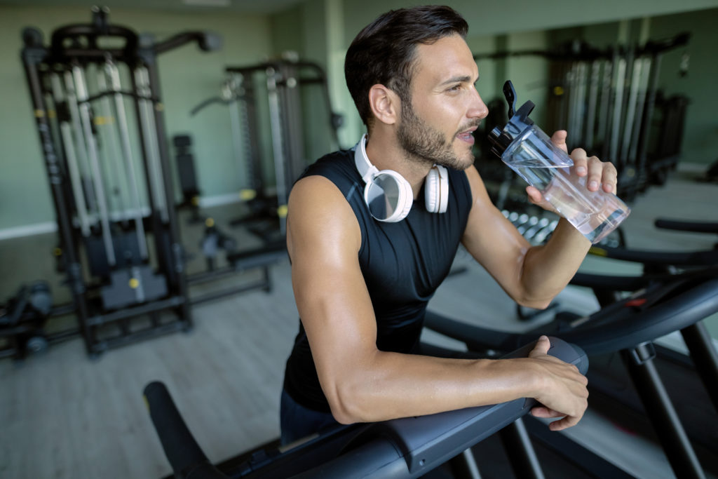 Thirsty athlete drinking water after running on treadmill at health club