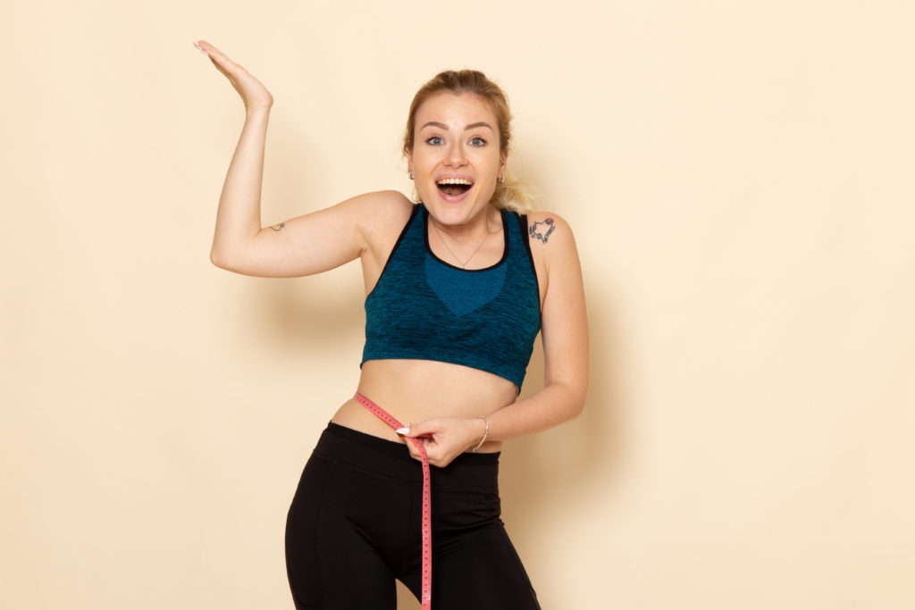 young female in sport outfit measuring her body