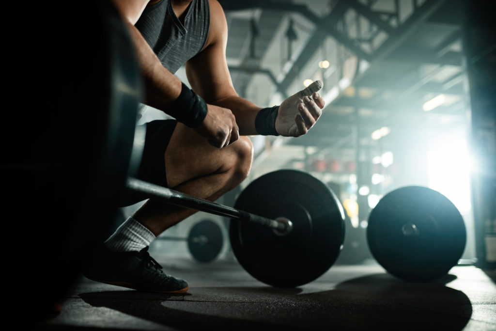 Low angle view of unrecognizable muscular build man preparing for lifting a barbell in a health club.