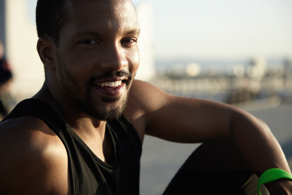 Handsome dark-skinned runner resting at seaside after activity in open air sitting on embankment