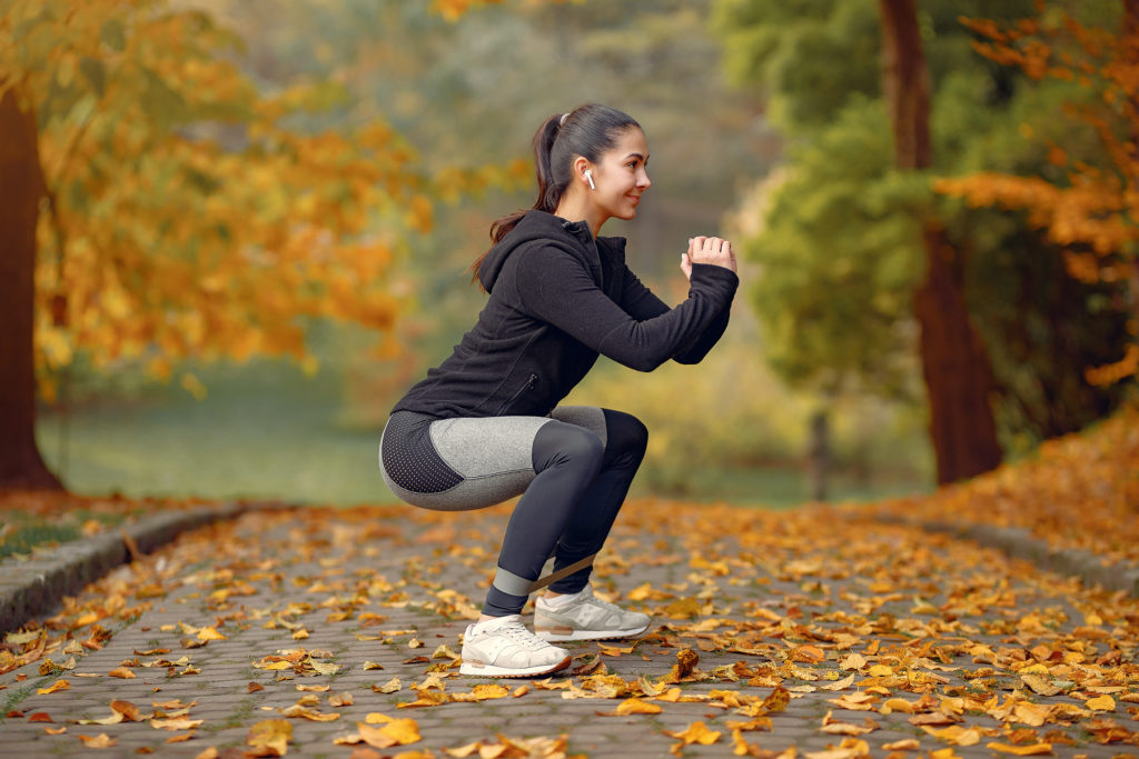 Sports girl in a black top training squats in a autumn park