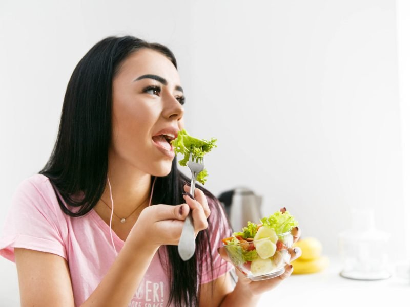 Smiling woman eats salad in the white kitchen